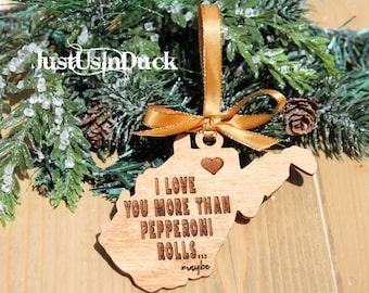 Puede incluir: Adorno de Navidad de madera con forma del estado de Virginia Occidental con el texto "I love you more than pepperoni rolls... maybe" grabado en él. El adorno está colgado de una cinta dorada.