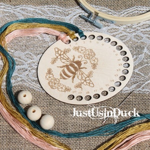 May include: A wooden embroidery thread organizer with 20 holes, featuring a bee and floral design. The organizer is labeled "Just Us in Duck". Three wooden beads and multiple strands of embroidery floss are included.