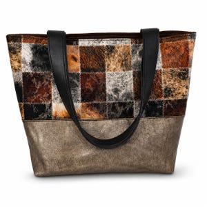 Peut inclure: Un sac fourre-tout avec un motif patchwork. La partie supérieure présente des carrés de matière texturée marron, noire et blanche. La partie inférieure est de couleur bronze métallique. Il a des poignées noires.