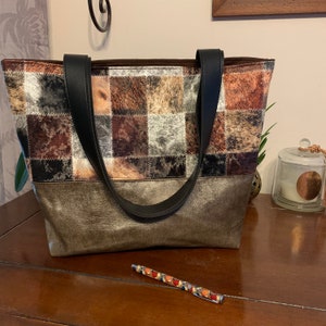 Peut inclure: Un sac fourre-tout en patchwork marron et noir avec des anses en cuir noir. Le sac a un fond métallique doré.