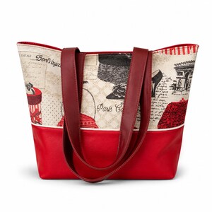 Peut inclure: Un sac fourre-tout rouge et crème avec des poignées bordeaux. Le sac présente un fond rouge et une partie supérieure crème avec un thème parisien, avec des illustrations de chapeaux, de la Tour Eiffel et les mots "Paris Cafe."