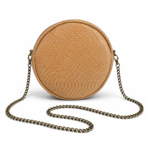 Peut inclure: Un sac bandoulière rond de couleur beige avec un motif peau de serpent. Il est doté d'une chaîne bronze et d'une fermeture éclair. Ce sac de couleur neutre est idéal pour un usage quotidien. Le diamètre du sac est d'environ 20 cm.