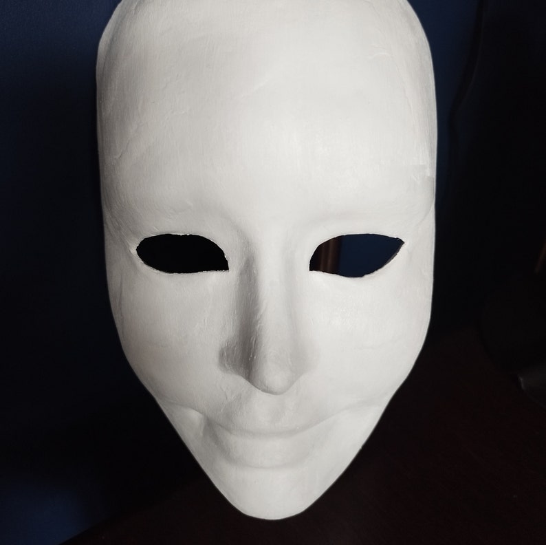 May include: A blank, white mask with eye openings and a smiling mouth. The mask is made of a smooth material and is designed to be worn on the face. It is a versatile item for costumes or artistic projects.