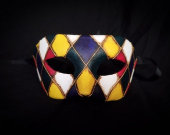 May include: A colorful masquerade mask with a diamond pattern in shades of yellow, red, white, green, and blue. The mask has two eye holes and is decorated with gold accents.