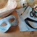 May include: A handmade, textured blue mask with eye openings, alongside art supplies like paint tubes, brushes, scissors, and black ribbon. The mask is the focal point, suggesting a crafting or DIY project. The items are arranged on a wooden surface.