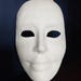 May include: A blank, white mask with eye holes and a smiling mouth. The mask is smooth and appears to be made of a solid material. The mask is designed to be worn on the face.