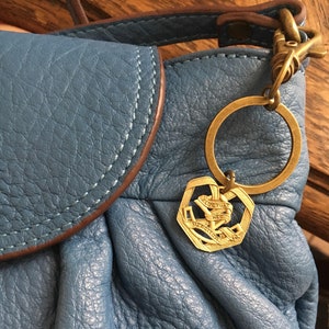 Peut inclure: Un sac à main en cuir bleu avec un porte-clés doré en forme de cœur avec le texte "VICTORIAN NECK MERGITOR".