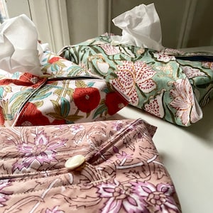 Peut inclure: Trois housses de boîte à mouchoirs avec des motifs floraux. La housse du haut est verte avec des fleurs blanches et roses. La housse du milieu est blanche avec des fleurs rouges et vertes. La housse du bas est rose avec des fleurs blanches et violettes.