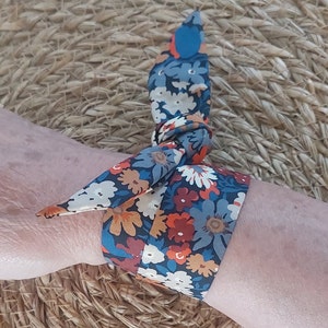 Könnte beinhalten: Ein blaues, orangefarbenes und weißes Armband aus Stoff mit Blumenmuster, das zu einer Schleife gebunden ist.