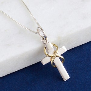 May include: A silver chain necklace with a silver cross pendant. The cross has a gold infinity symbol wrapped around it.