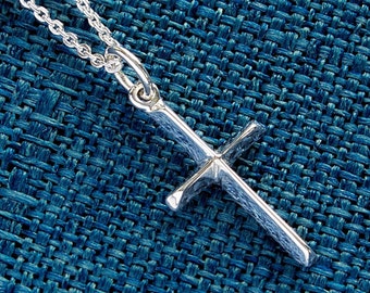 May include: A silver cross pendant on a silver chain necklace. The pendant is a simple, classic design with a slightly textured surface.
