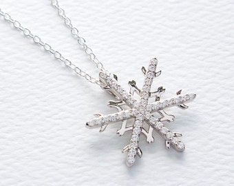 May include: A silver snowflake pendant necklace with clear cubic zirconia stones. The snowflake is detailed and intricate, with a delicate chain.