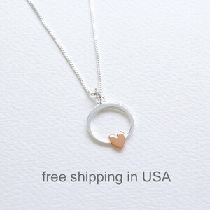 Puede incluir: Un collar de cadena de plata con un colgante circular de plata y un pequeño dije de corazón de oro rosa.