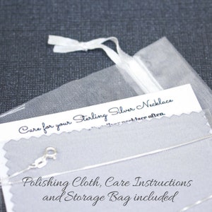 K&ouml;nnte beinhalten: Nahaufnahme einer silbernen Halskette mit einer Pflegekarte und einem Poliertuch. Die Karte lautet "Care for your Sterling Silver Necklace" und "Polishing Cloth, Care Instructions and Storage Bag included".