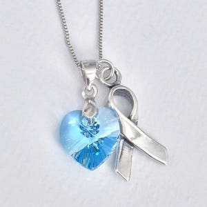 May include: A silver necklace with a light blue crystal heart charm and a silver ribbon charm.
