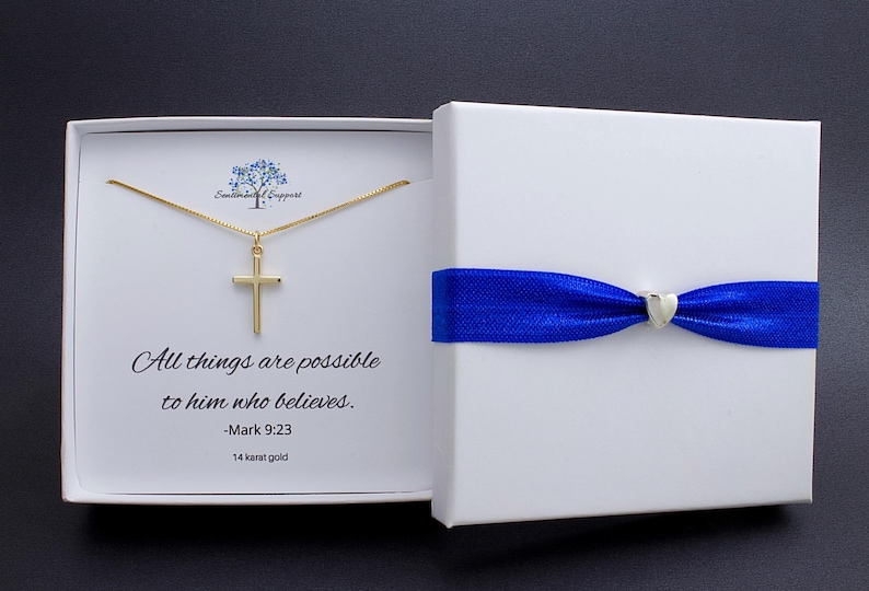 May include: A gold cross pendant necklace inside a white gift box with a blue ribbon. The box is open, revealing the necklace and text that reads "All things are possible to him who believes. -Mark 9:23". The necklace is 14 karat gold.