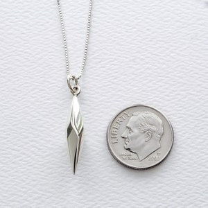 Puede incluir: Un collar de plata con un colgante geom&eacute;trico en forma de l&aacute;grima puntiaguda y alargada. El colgante es aproximadamente del tama&ntilde;o de una moneda de diez c&eacute;ntimos.