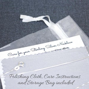 May include: A close-up of a white organza bag with a silver necklace inside. The bag is labeled "Care for your Sterling Silver Necklace" and includes instructions for polishing and storage.
