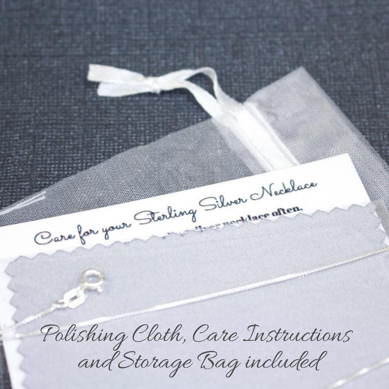 May include: A close-up of a white organza bag with a silver necklace inside. The bag is labeled "Care for your Sterling Silver Necklace" and includes instructions for polishing and storage.