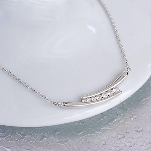 May include: A silver necklace with a curved bar pendant set with clear cubic zirconia stones.
