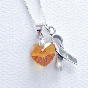 Può includere: Una collana d'argento con un ciondolo a forma di cuore in cristallo arancione e un ciondolo a nastro d'argento.