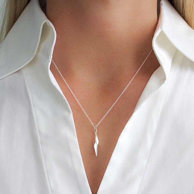 Puede incluir: Un collar de plata con un colgante geom&eacute;trico en forma de punta afilada.