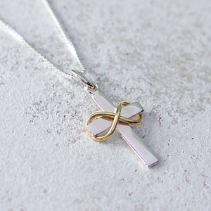 Puede incluir: Un collar de cadena de plata con un colgante de cruz de plata y oro. La cruz tiene un diseño de símbolo de infinito en oro.