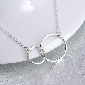 May include: A silver necklace with two interlocking circles. The circles are connected at the top and hang from a delicate chain.