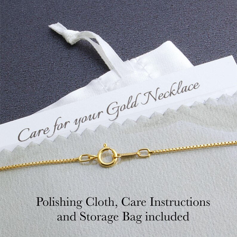 May include: Close-up of a gold necklace with a delicate chain and clasp. A white bag with the text "Care for your Gold Necklace" is visible. The image also includes a polishing cloth, care instructions, and a storage bag.