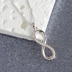 May include: Silver infinity pendant necklace with clear cubic zirconia stones. The pendant is on a silver chain.