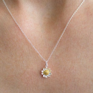 May include: A silver chain necklace with a small gold and silver daisy pendant.