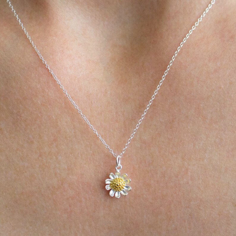 May include: A silver chain necklace with a small gold and silver daisy pendant.