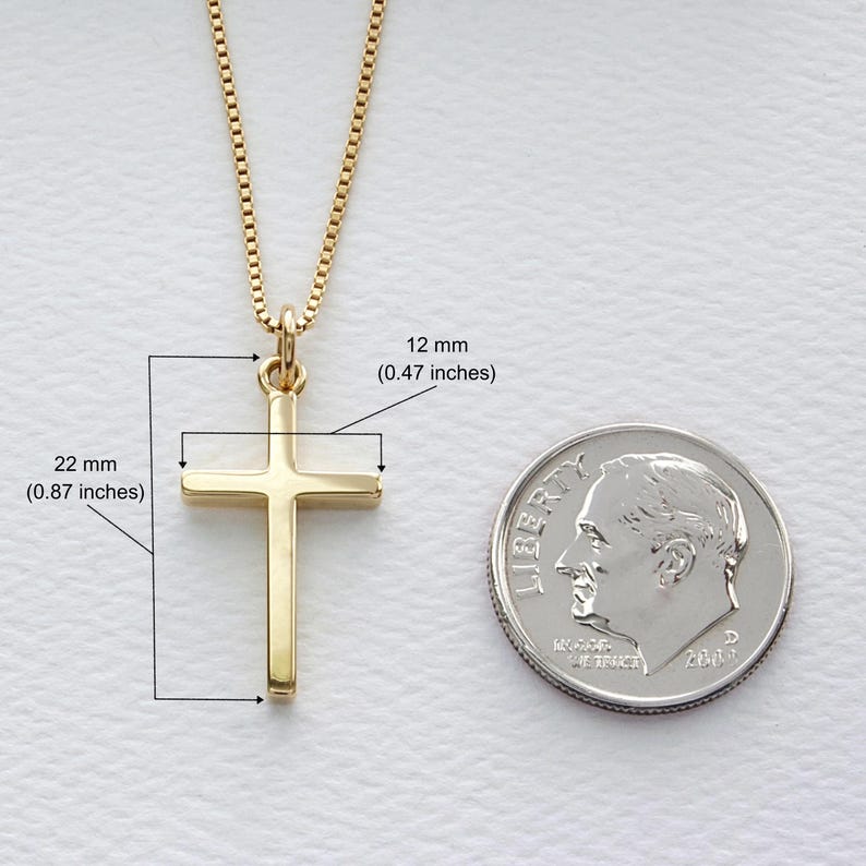 May include: A gold-colored cross pendant on a gold chain. The cross measures 0.87 inches wide and 0.47 inches high. A US dime is next to the cross for size comparison. The chain has a box link design.