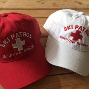May include: Two red and white baseball caps with the text "Ski Patrol Mountain Rescue" and a red cross.
