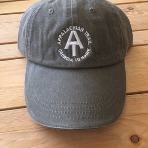 Op de afbeelding: Een grijze baseballpet met het Appalachian Trail-logo geborduurd op de voorkant. Het logo is wit en bevat de letters "AT" en de woorden "Appalachian Trail, Georgia to Maine".