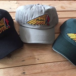 Op de afbeelding: Drie baseballpetten met het Indian Motorcycle logo. De petten zijn zwart, grijs en groen.
