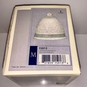 May include: A white porcelain bell ornament with a green base and the year 1992 inscribed on it. The box is labelled "Campanita Navidad 92" and "1992 Christmas Bell".