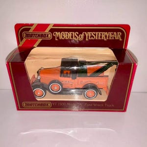 May include: A Matchbox Models of Yesteryear toy car, a 1930 Model A Ford Wreck Truck, in an orange and black color scheme. The truck has a tow hook and the words "Arrow Motor Sales" and "Quality Cars" on the side. The box is red and gold with the Matchbox logo.