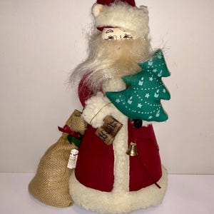 May include: A Santa Claus figure in a red coat with white faux fur trim and a matching hat. He holds a green Christmas tree and a burlap sack. A small gold bell hangs from his coat.
