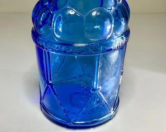 Peut inclure: Un récipient en verre bleu cobalt avec un design unique. La partie supérieure présente un motif texturé en forme de bulles, tandis que la section inférieure présente un motif géométrique en losange. Il s'agit probablement d'une pièce décorative ou d'un bocal de rangement.