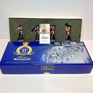 May include: A W. Britain Golden Jubilee Series set featuring four miniature toy soldiers in red and black uniforms, presented in a blue box with a black and white historical procession image and the text Elizabeth II 2nd June 1953.