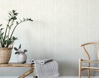 May include: A wooden bench with a grey knitted throw blanket on top. A potted plant sits on the bench. A wicker basket with a potted plant sits on the floor. A wooden chair with a woven seat sits in the background. The wall behind the bench is covered in a white and beige striped wallpaper.