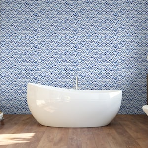 May include: A white bathtub sits in front of a wall with a blue and white geometric pattern. The pattern is made up of repeating semi-circles.