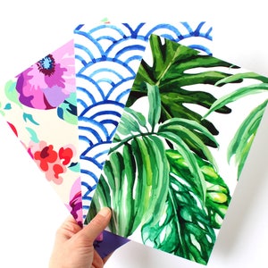 May include: Four different patterned sheets of paper. One sheet has a floral pattern with pink, red, and purple flowers on a cream background. Another sheet has a blue and white geometric pattern. The third sheet has a green and white tropical leaf pattern. The fourth sheet has a purple and blue floral pattern.