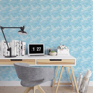 Pu&ograve; includere: Un ufficio domestico con una carta da parati a motivi di onde blu e bianche. Una scrivania in legno con due cassetti e una sedia da ufficio grigia. Un computer portatile con un orologio digitale che mostra le 1:27. Una lampada con un paralume nero e una pila di libri sono sulla scrivania.