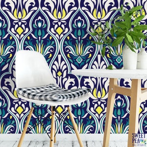 May include: A white chair with a black and white checkered cushion sits in front of a wall with a navy blue, white, yellow, and teal floral pattern. A small white table and a vase with green leaves are also visible.