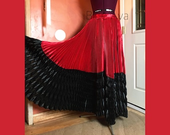 May include: A red and black pleated skirt with a ruffled hem. The skirt is made of a shiny fabric and has a wide waistband.