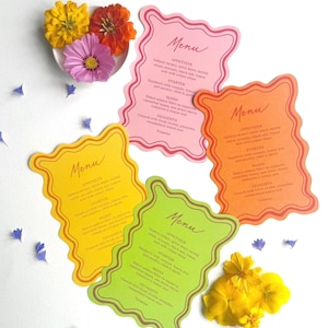Pode incluir: Quatro cartões de menu coloridos com uma borda ondulada, cada um com a palavra "Menu" no topo. Os cartões são rosa, laranja, amarelo e verde. Os menus listam aperitivos, entradas, pratos principais e sobremesas. Flores e pétalas espalhadas.