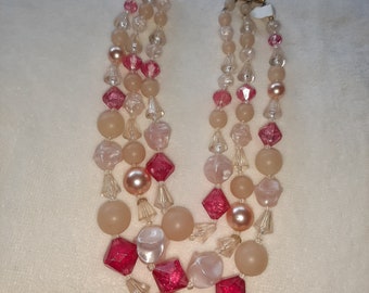 May include: A three-strand necklace with pink, white, and red beads. The beads are various shapes and sizes, including round, square, and teardrop.
