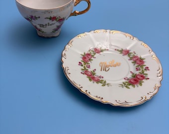 Peut inclure: Un service à thé blanc avec un motif floral et des bordures dorées. La tasse et la soucoupe sont décorées de roses roses et du mot "Mother". La poignée de la tasse est dorée.